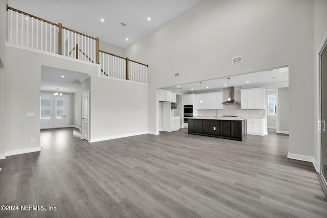 unfurnished living room with baseboards, visible vents, a notable chandelier, and wood finished floors