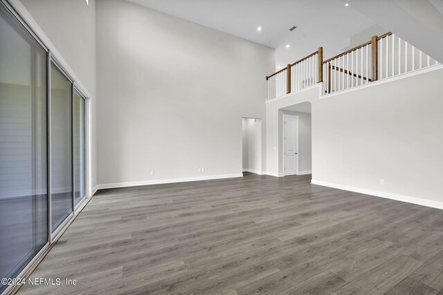 unfurnished living room with a high ceiling, recessed lighting, wood finished floors, and baseboards