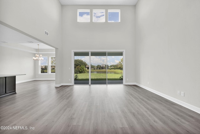 unfurnished living room with baseboards, visible vents, wood finished floors, a high ceiling, and a notable chandelier