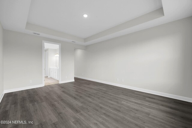 empty room with a tray ceiling, wood finished floors, visible vents, and baseboards