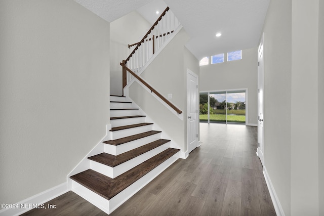 staircase with a high ceiling, baseboards, and wood finished floors