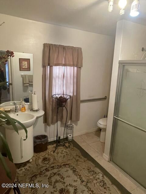 bathroom with tile flooring, toilet, and a shower with shower door