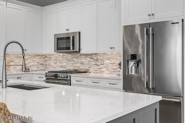 kitchen with tasteful backsplash, light stone countertops, white cabinetry, and high quality appliances