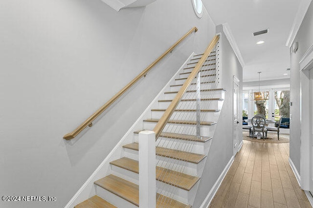 staircase with light hardwood / wood-style flooring, a notable chandelier, and crown molding