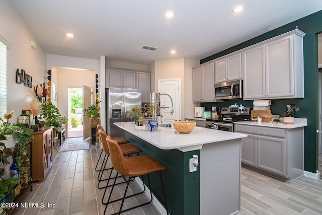 kitchen featuring a kitchen breakfast bar, a center island with sink, light hardwood / wood-style flooring, appliances with stainless steel finishes, and gray cabinetry