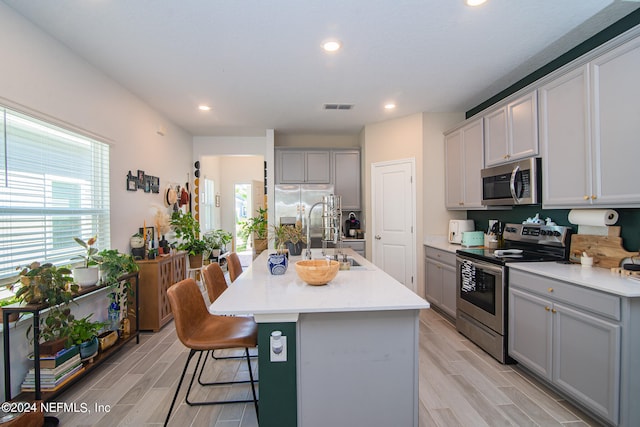 kitchen with appliances with stainless steel finishes, a kitchen island with sink, gray cabinets, and a breakfast bar