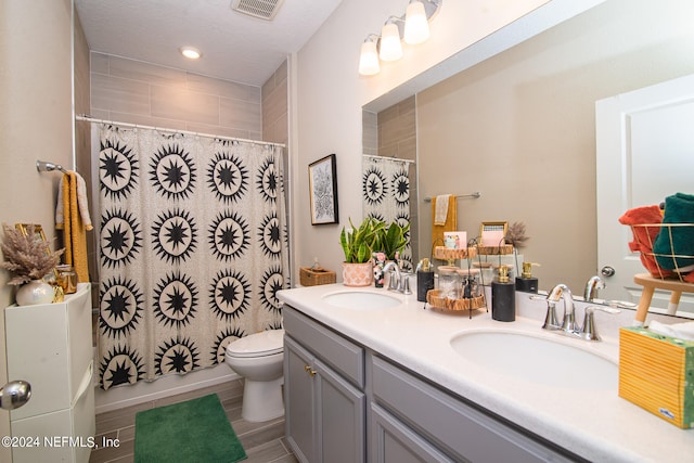 bathroom featuring a textured ceiling, toilet, and dual bowl vanity