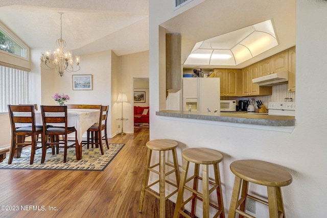 kitchen with hardwood / wood-style floors, white appliances, backsplash, lofted ceiling, and a chandelier