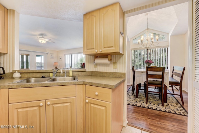 kitchen with light brown cabinetry, light wood-type flooring, ceiling fan with notable chandelier, sink, and lofted ceiling