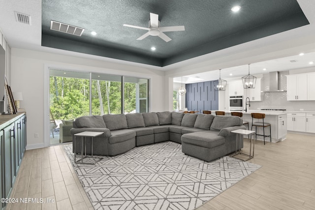 living area with a tray ceiling, visible vents, and light wood-style flooring