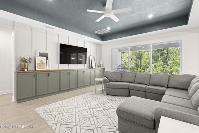 living area featuring light wood-style floors, visible vents, a tray ceiling, and a textured ceiling