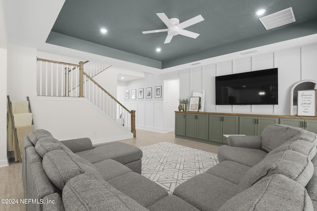 living room featuring light wood finished floors, visible vents, a ceiling fan, stairs, and a decorative wall