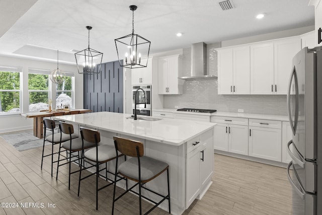 kitchen with stainless steel appliances, a sink, visible vents, backsplash, and wall chimney exhaust hood