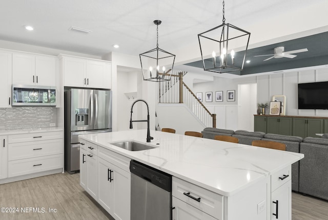 kitchen with light wood-style flooring, stainless steel appliances, a sink, open floor plan, and decorative backsplash