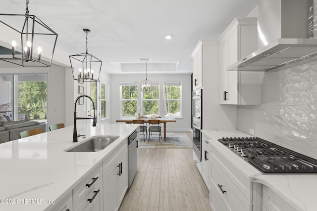 kitchen with decorative backsplash, appliances with stainless steel finishes, white cabinetry, a sink, and wall chimney range hood