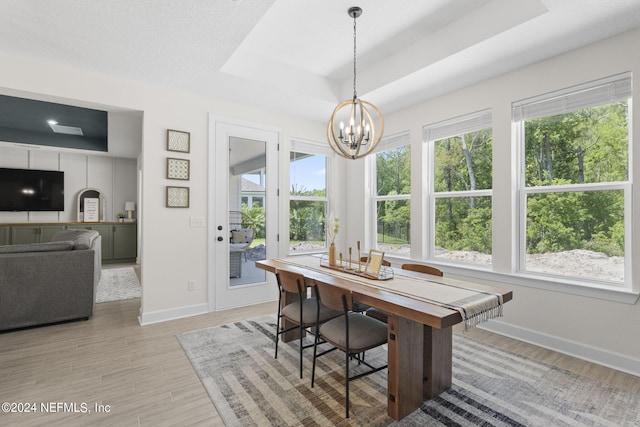 dining area with baseboards, light wood-type flooring, a raised ceiling, and a notable chandelier