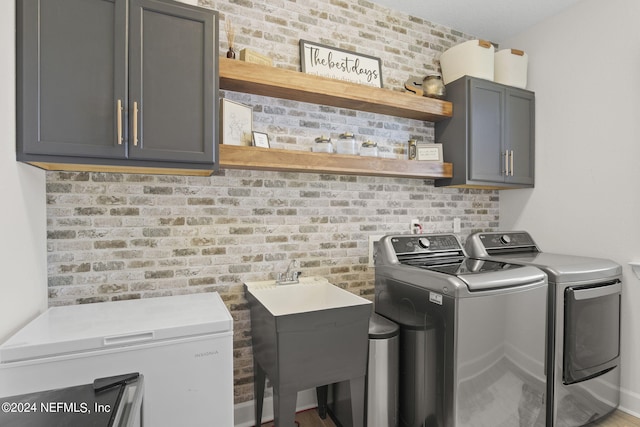 laundry room with brick wall, independent washer and dryer, a sink, and cabinet space