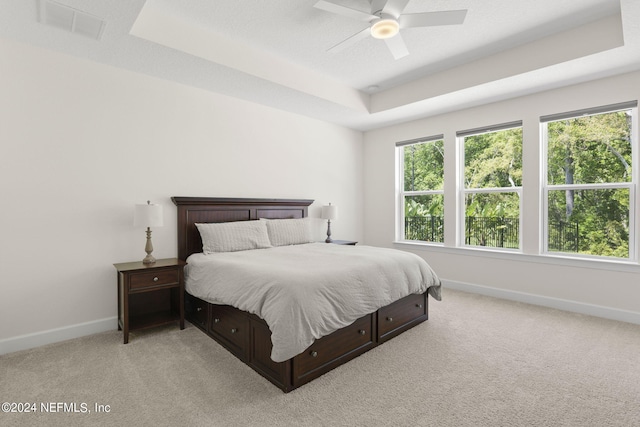 bedroom featuring a tray ceiling, light colored carpet, visible vents, and baseboards