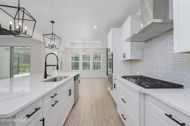 kitchen featuring decorative backsplash, appliances with stainless steel finishes, white cabinets, a sink, and wall chimney range hood