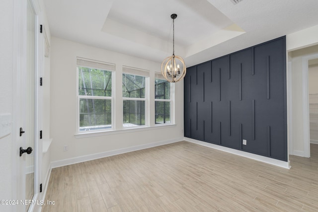 empty room featuring baseboards, light wood-type flooring, a raised ceiling, and a notable chandelier