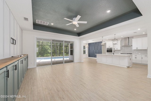 unfurnished living room featuring light wood finished floors, visible vents, a raised ceiling, and ceiling fan with notable chandelier