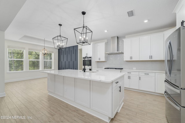 kitchen featuring a sink, visible vents, wall chimney range hood, freestanding refrigerator, and decorative backsplash