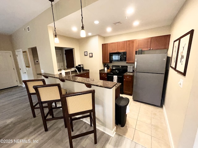 kitchen featuring a kitchen breakfast bar, black appliances, hanging light fixtures, kitchen peninsula, and dark stone counters