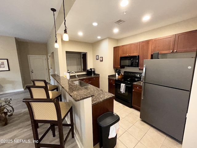 kitchen featuring sink, decorative light fixtures, dark stone countertops, black appliances, and a breakfast bar