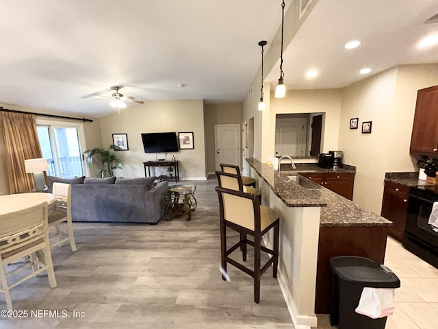 kitchen featuring hanging light fixtures, ceiling fan, a kitchen bar, range with electric stovetop, and light hardwood / wood-style flooring