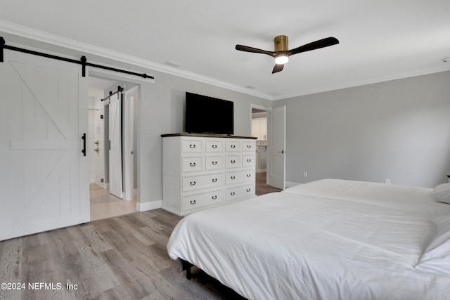 bedroom featuring light wood-type flooring, ensuite bathroom, ornamental molding, ceiling fan, and a barn door