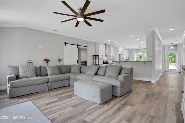 living room featuring ceiling fan, a barn door, ornamental molding, and light hardwood / wood-style flooring