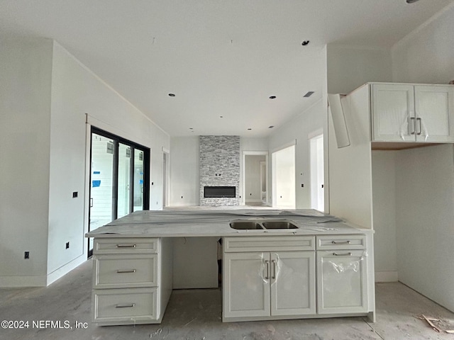 kitchen with a stone fireplace, light stone countertops, sink, and white cabinets