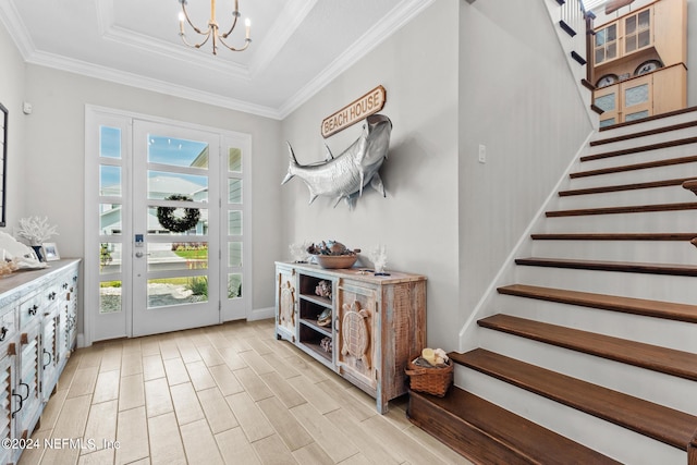 entryway with a raised ceiling, ornamental molding, light hardwood / wood-style flooring, and a chandelier