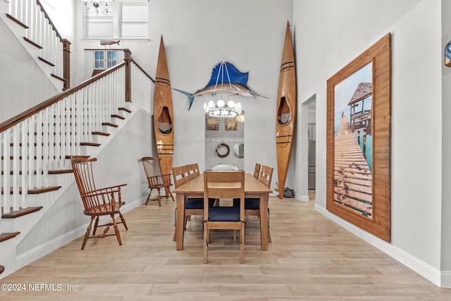 dining room with a towering ceiling, light wood-type flooring, and a notable chandelier