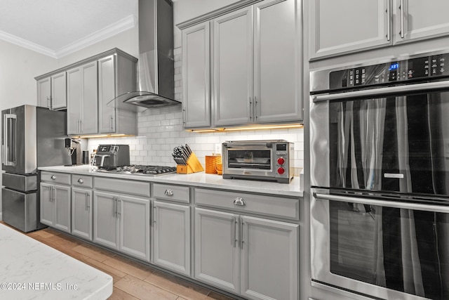 kitchen with wall chimney exhaust hood, stainless steel appliances, light stone counters, crown molding, and light hardwood / wood-style floors