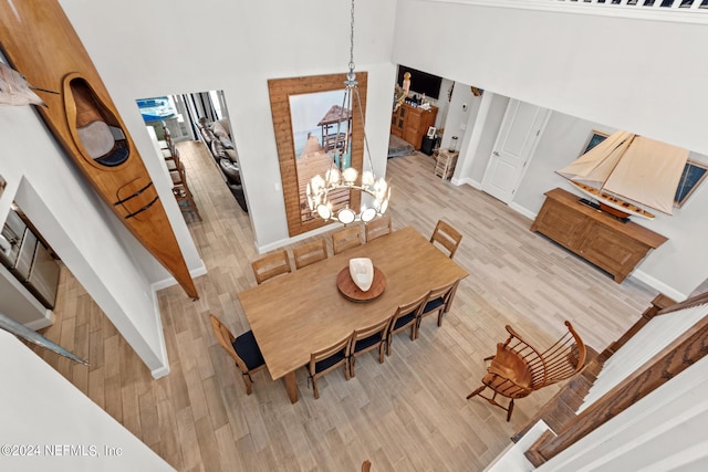 dining room with light wood-type flooring, a towering ceiling, and an inviting chandelier