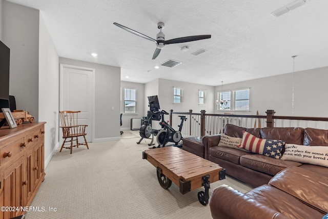 living room with ceiling fan with notable chandelier, a textured ceiling, light colored carpet, and a wealth of natural light