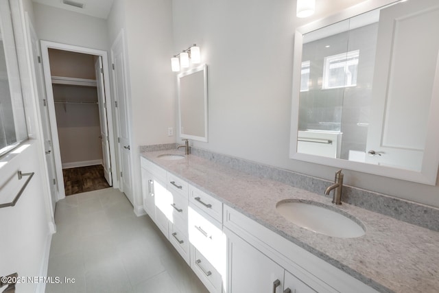 bathroom featuring double vanity, visible vents, a walk in closet, and a sink