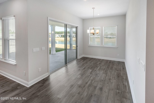 unfurnished dining area featuring dark wood-style floors, baseboards, and a notable chandelier