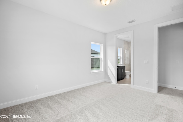 unfurnished bedroom featuring light carpet and ensuite bath