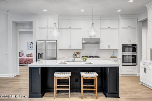 kitchen with a kitchen island with sink, light hardwood / wood-style flooring, appliances with stainless steel finishes, decorative light fixtures, and white cabinetry