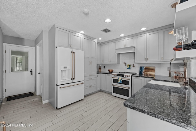 kitchen with dark stone countertops, high end appliances, white cabinetry, tasteful backsplash, and hanging light fixtures