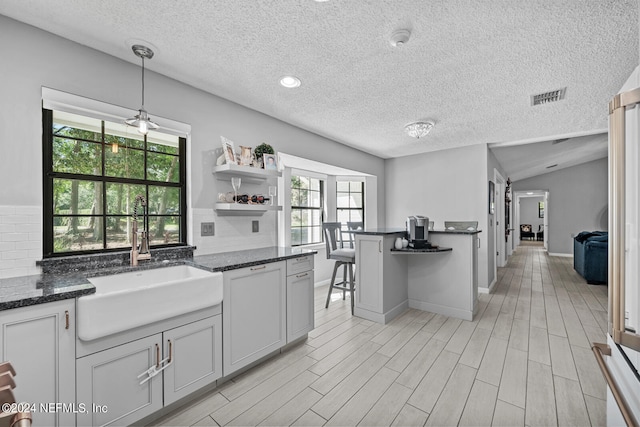 kitchen featuring tasteful backsplash, sink, a textured ceiling, lofted ceiling, and hanging light fixtures