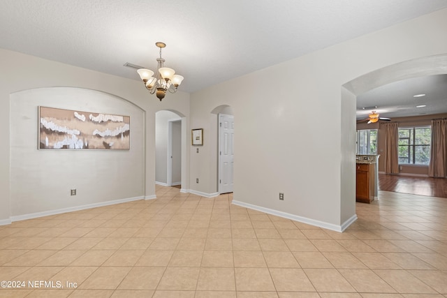 spare room featuring visible vents, baseboards, arched walkways, light tile patterned flooring, and ceiling fan with notable chandelier