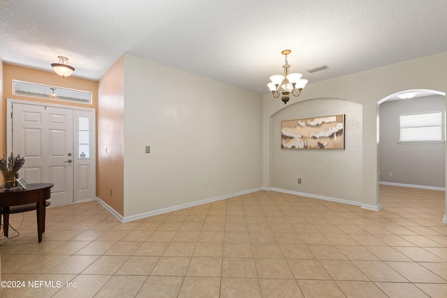 tiled foyer entrance featuring a textured ceiling and a chandelier