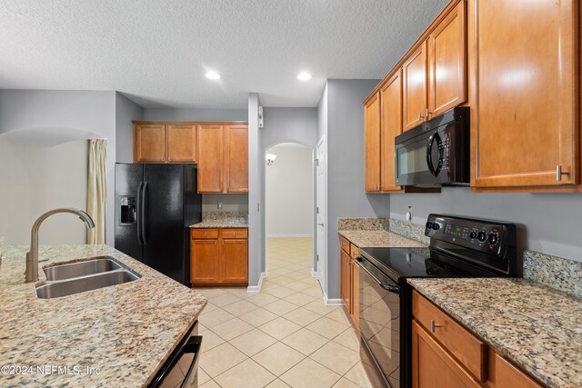 kitchen with arched walkways, light tile patterned floors, a sink, light stone countertops, and black appliances