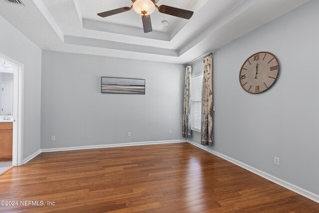 spare room featuring ceiling fan, wood finished floors, visible vents, baseboards, and a raised ceiling