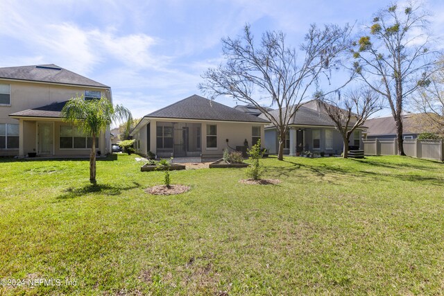 back of property with a sunroom, fence, stucco siding, and a yard