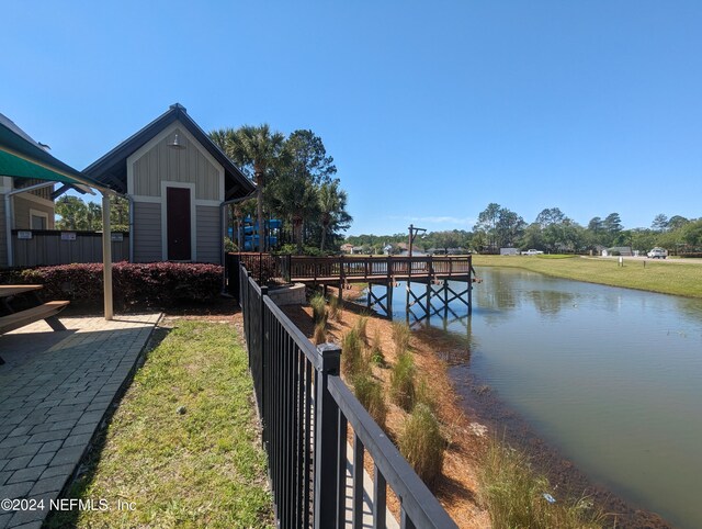 view of dock featuring a yard, a water view, and fence