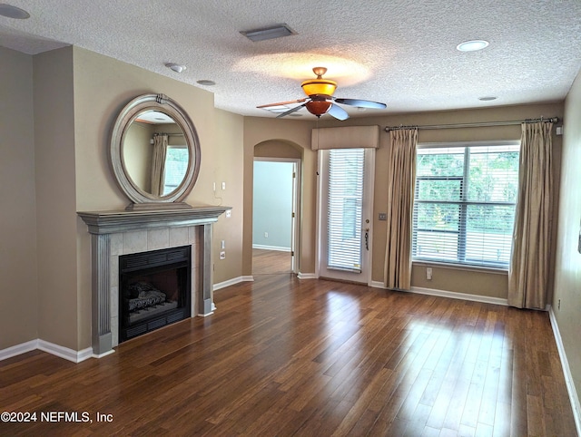 unfurnished living room featuring visible vents, a tiled fireplace, a ceiling fan, wood finished floors, and baseboards